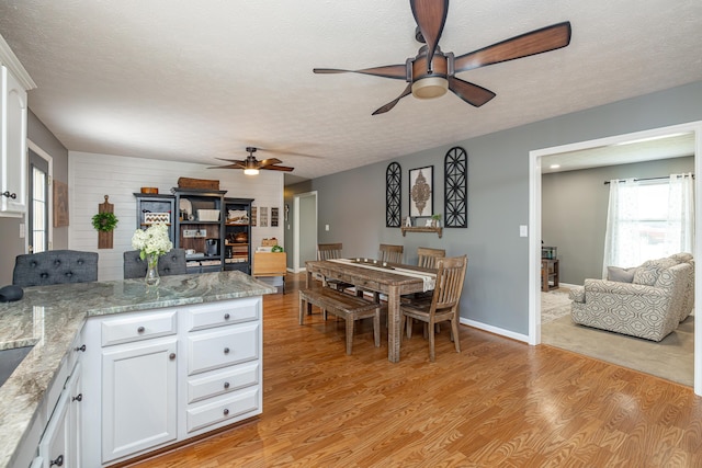 dining space with a textured ceiling, ceiling fan, baseboards, and light wood-style floors