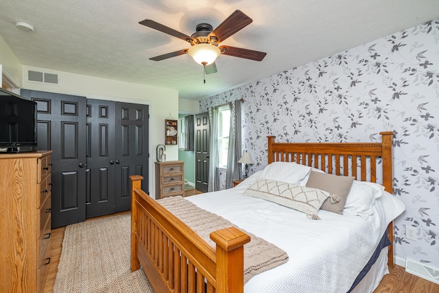 bedroom featuring light wood finished floors, a closet, visible vents, a textured ceiling, and wallpapered walls