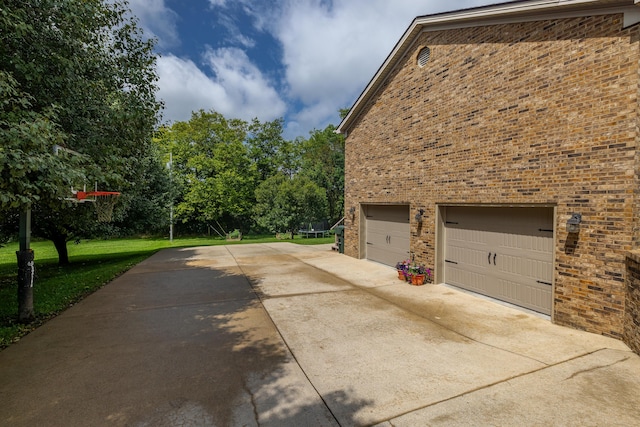 view of side of property with a garage, concrete driveway, a lawn, and brick siding