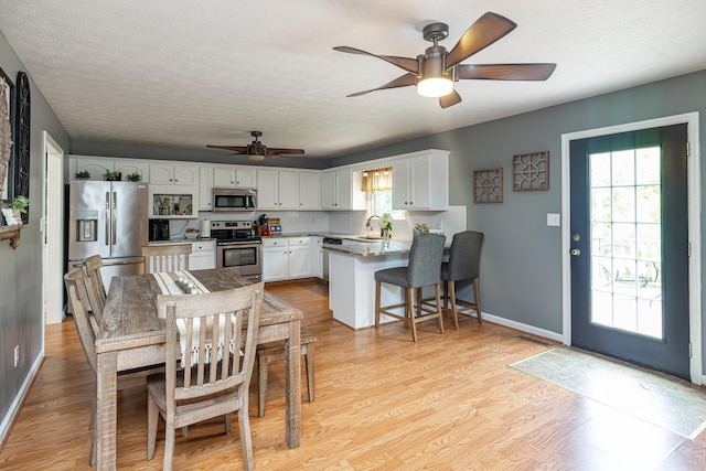 dining room with light wood-style floors, ceiling fan, baseboards, and a textured ceiling