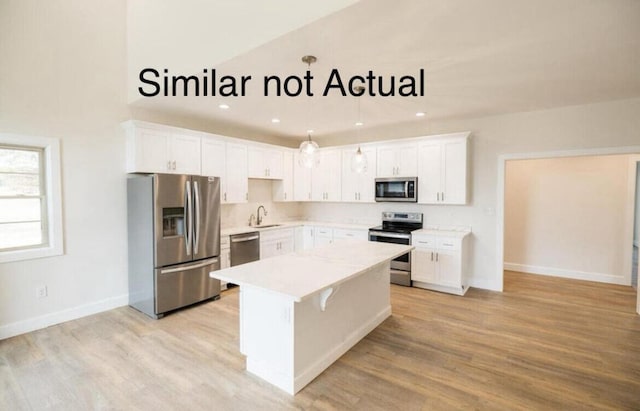 kitchen featuring hanging light fixtures, white cabinetry, stainless steel appliances, a center island, and light hardwood / wood-style floors