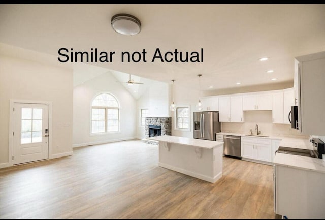 kitchen with a stone fireplace, stainless steel appliances, vaulted ceiling, and a healthy amount of sunlight