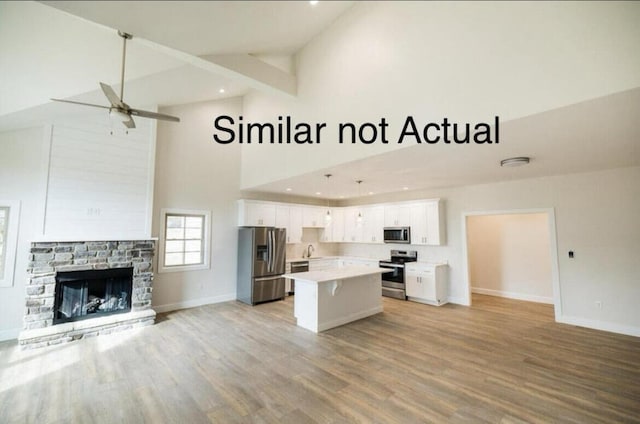 kitchen featuring ceiling fan, high vaulted ceiling, white cabinetry, stainless steel appliances, and a center island