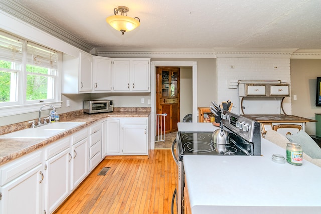 kitchen with light wood-type flooring, stainless steel electric stove, ornamental molding, white cabinets, and sink