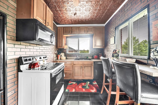 kitchen featuring brick wall, sink, dark tile patterned floors, ornamental molding, and black appliances