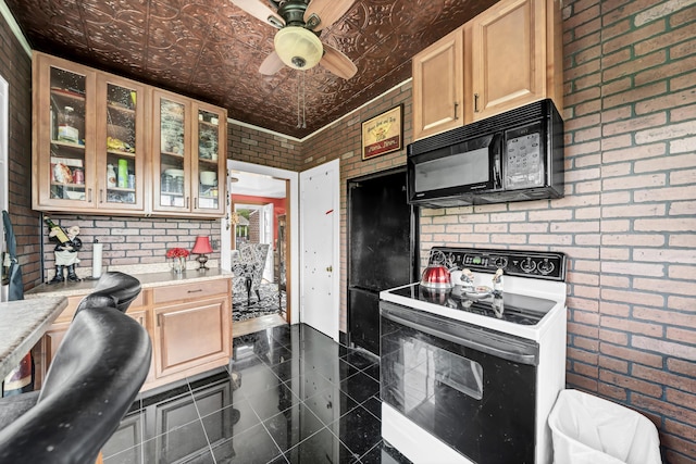 kitchen with light brown cabinetry, electric range oven, ceiling fan, and brick wall