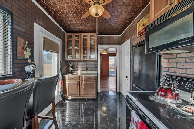 kitchen with light stone counters, ornamental molding, ceiling fan, brick wall, and black appliances