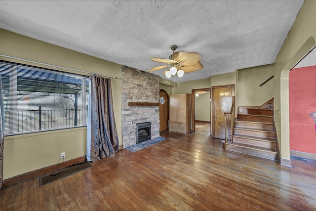 unfurnished living room featuring dark wood-type flooring, ceiling fan, a fireplace, and a textured ceiling