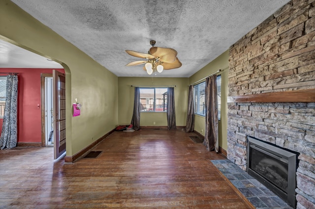 unfurnished living room with ceiling fan, dark wood-type flooring, a textured ceiling, and a fireplace