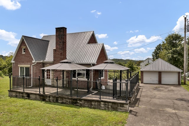 rear view of house featuring a gazebo, a garage, an outdoor structure, and a lawn