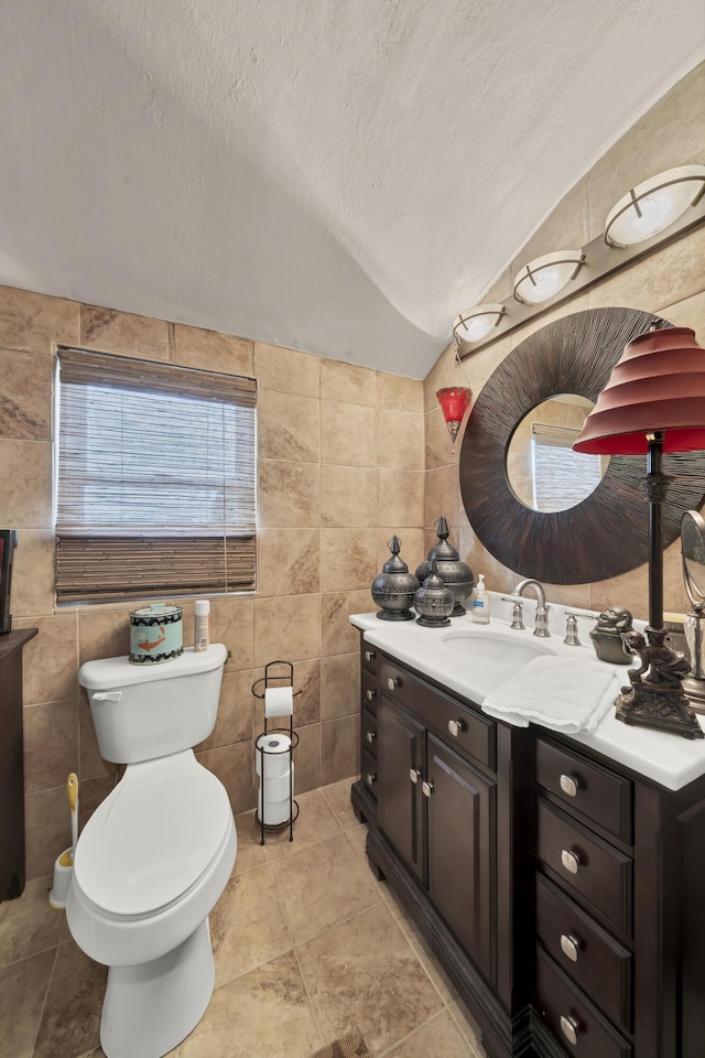 bathroom featuring toilet, vaulted ceiling, a textured ceiling, tile walls, and vanity