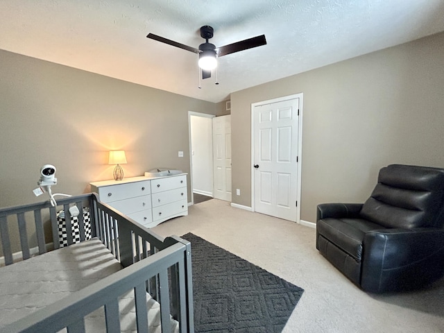 carpeted bedroom with a nursery area, ceiling fan, and a textured ceiling