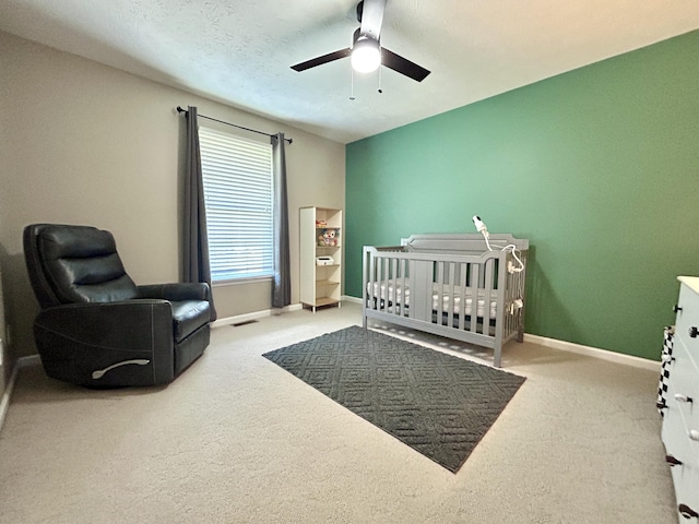 carpeted bedroom with a textured ceiling, a nursery area, and ceiling fan