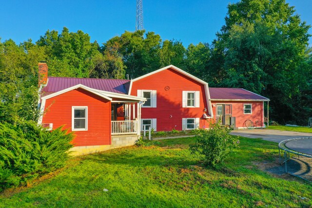 rear view of property with a trampoline, a yard, and covered porch