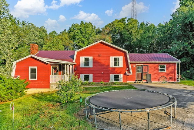 rear view of property with covered porch, a lawn, and a trampoline