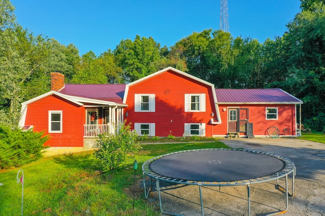 rear view of house featuring a trampoline, a porch, and a yard