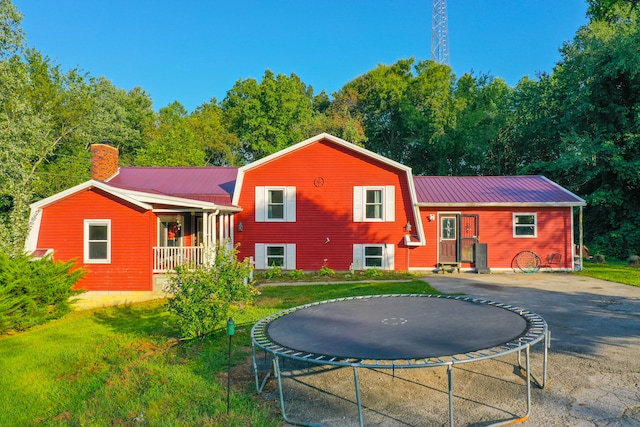 back of property with a trampoline, a porch, and a yard