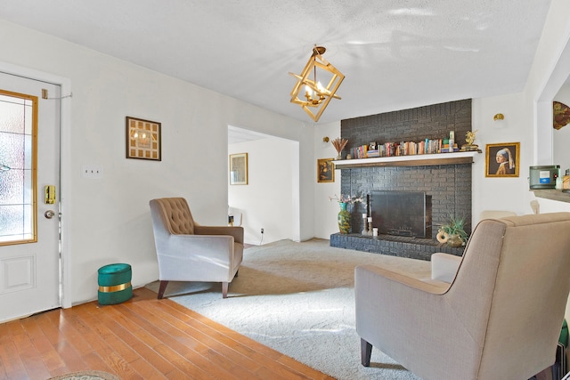 living room with wood-type flooring, a brick fireplace, an inviting chandelier, and a textured ceiling