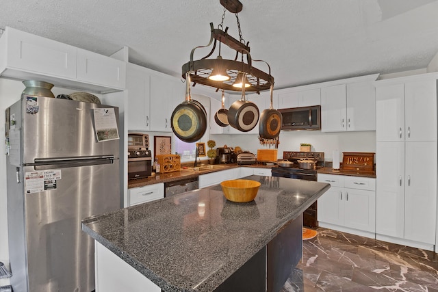 kitchen with stainless steel appliances, hanging light fixtures, a textured ceiling, a kitchen island, and white cabinets