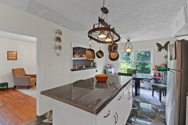 kitchen with hanging light fixtures, dark stone counters, stainless steel refrigerator, and white cabinetry