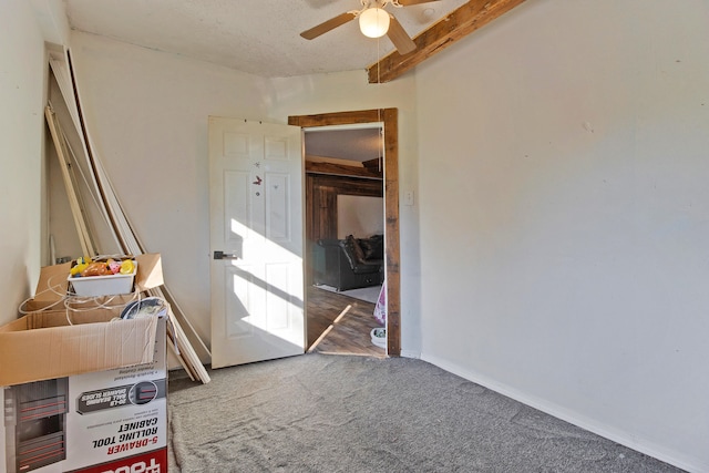 unfurnished bedroom with ceiling fan, beam ceiling, and carpet flooring