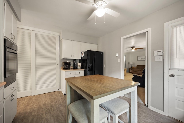 kitchen featuring dark wood-type flooring, ceiling fan, white cabinetry, wall oven, and black fridge with ice dispenser