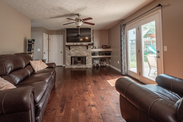 living room featuring ceiling fan, a stone fireplace, dark wood-type flooring, and a textured ceiling