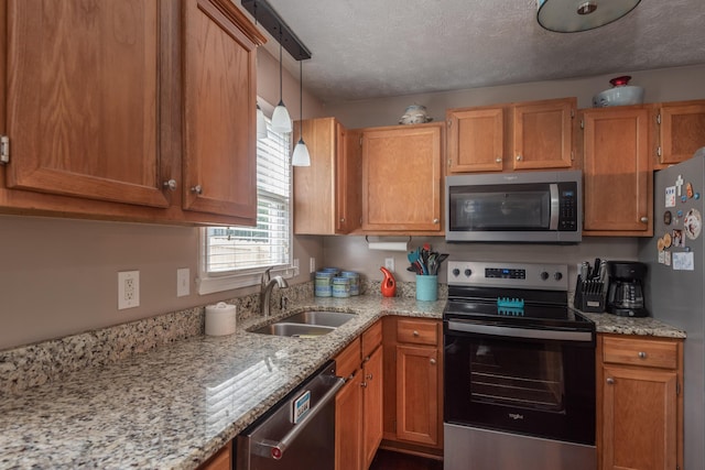 kitchen with sink, light stone counters, decorative light fixtures, a textured ceiling, and appliances with stainless steel finishes