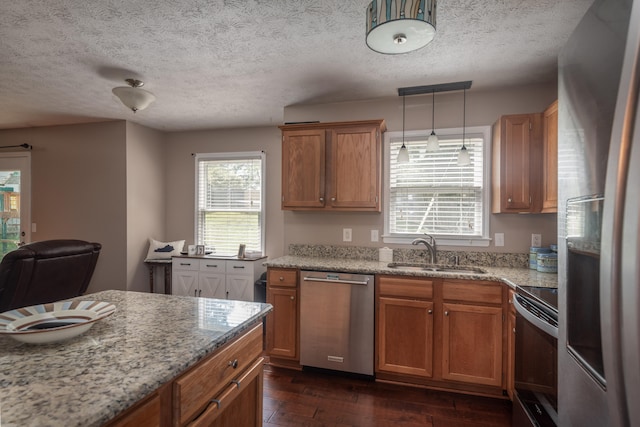 kitchen with dark wood-type flooring, light stone countertops, appliances with stainless steel finishes, pendant lighting, and sink