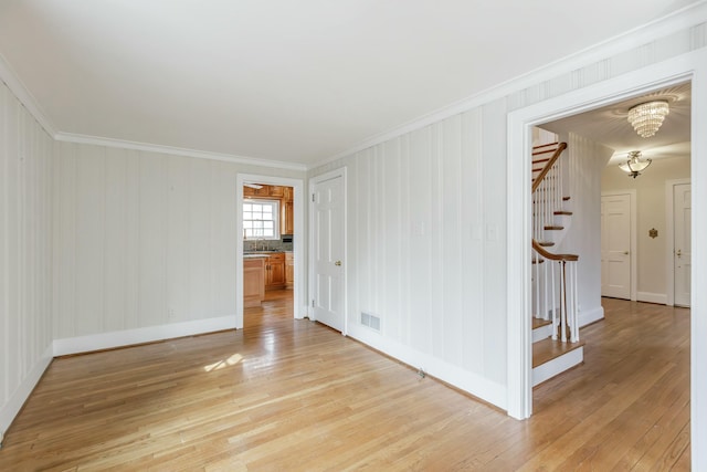 empty room with an inviting chandelier, ornamental molding, and light wood-type flooring