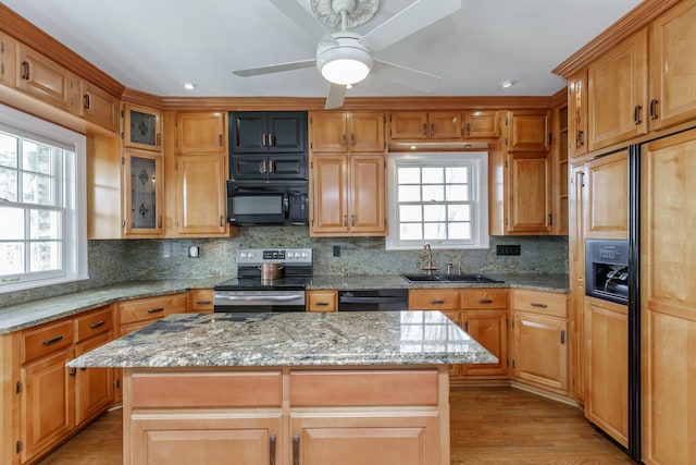 kitchen featuring a center island, sink, light stone counters, and black appliances