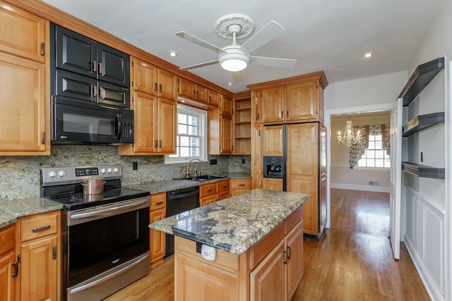 kitchen with sink, a center island, black appliances, light stone countertops, and decorative backsplash