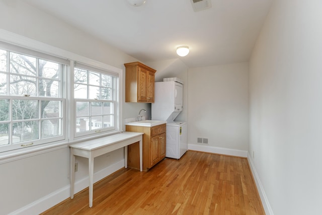 washroom with stacked washer and dryer, sink, light hardwood / wood-style floors, and cabinets