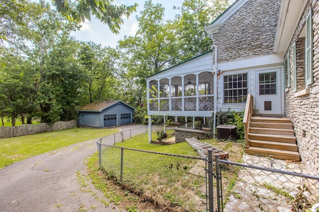 exterior space featuring central AC, a garage, an outbuilding, a yard, and a sunroom