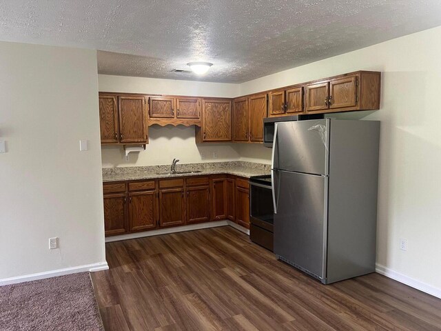 kitchen with light stone counters, sink, dark wood-type flooring, and stainless steel appliances