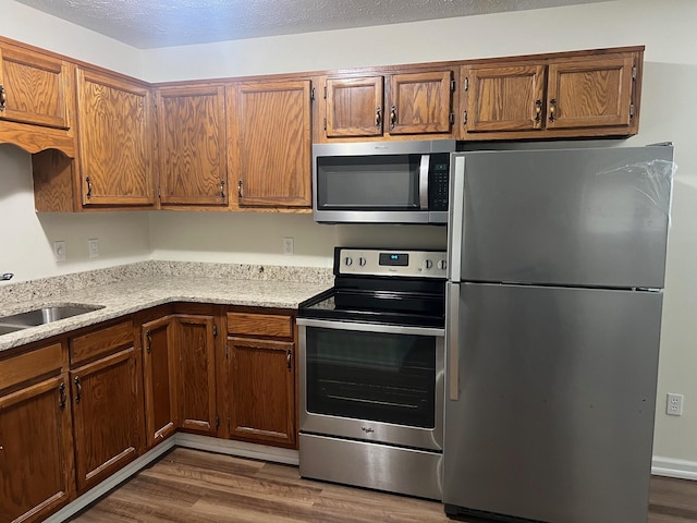 kitchen with appliances with stainless steel finishes, sink, hardwood / wood-style floors, and a textured ceiling