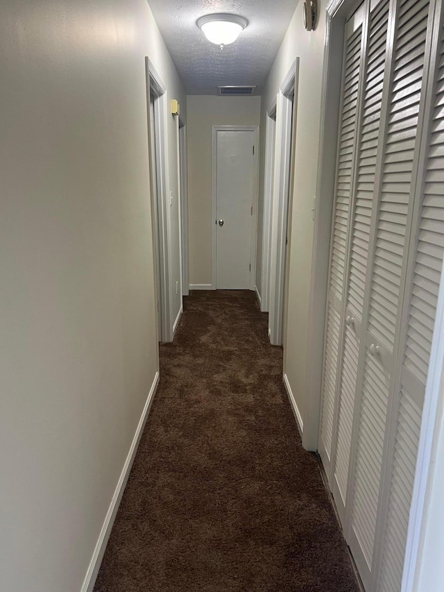 corridor featuring dark colored carpet and a textured ceiling