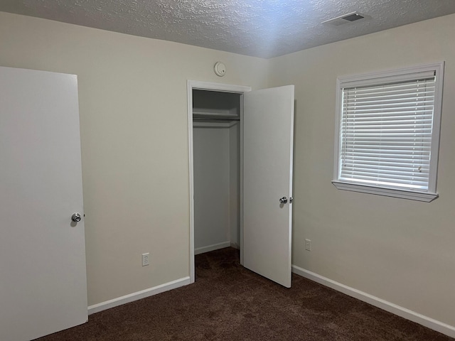 unfurnished bedroom with dark colored carpet, a textured ceiling, and a closet