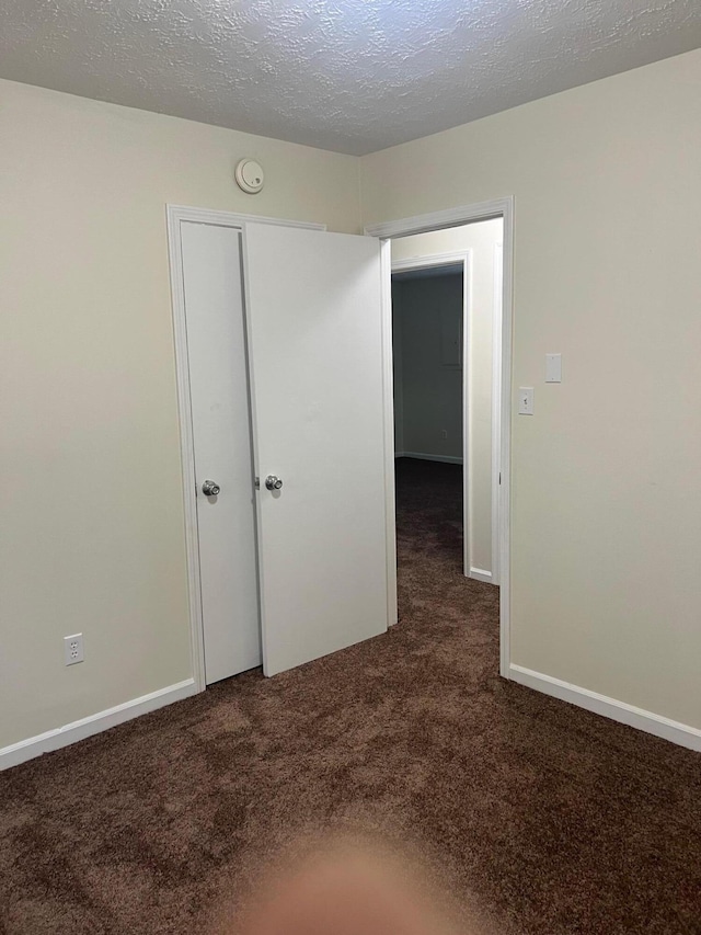 unfurnished bedroom featuring a textured ceiling and dark colored carpet