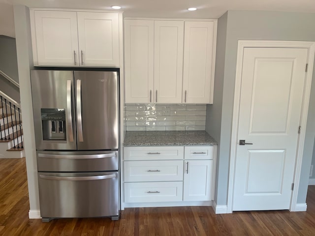 kitchen with dark wood-type flooring, stainless steel refrigerator with ice dispenser, backsplash, and white cabinetry