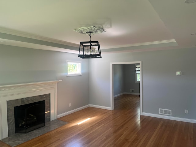 unfurnished living room with a premium fireplace, a tray ceiling, ornamental molding, and hardwood / wood-style flooring