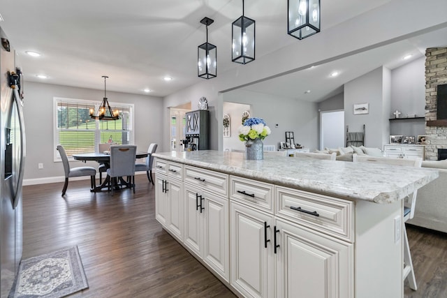 kitchen with hanging light fixtures, white cabinets, light stone countertops, lofted ceiling, and dark wood-type flooring