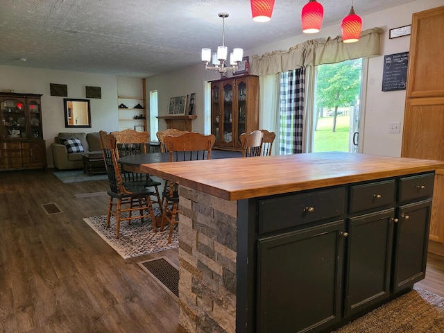 kitchen with dark hardwood / wood-style flooring, a textured ceiling, butcher block counters, a chandelier, and a kitchen island