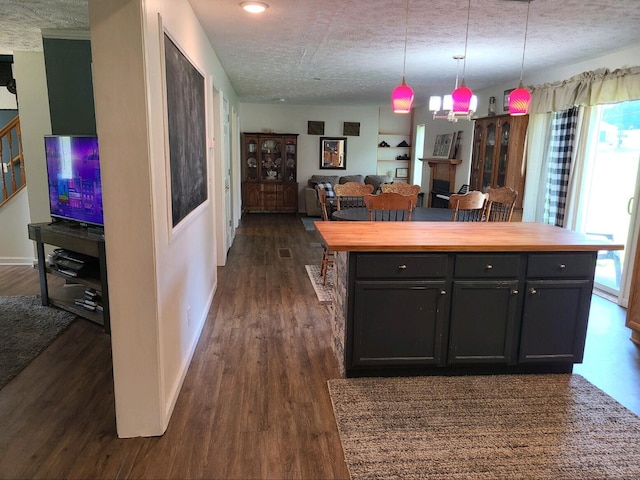 kitchen with a textured ceiling, dark hardwood / wood-style floors, hanging light fixtures, and butcher block counters