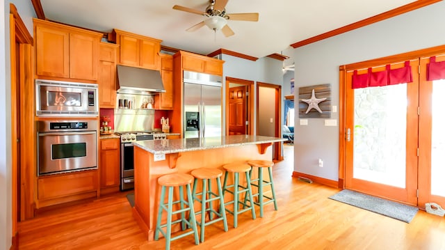 kitchen featuring light wood-type flooring, built in appliances, ceiling fan, stone counters, and a center island