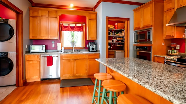 kitchen with premium range hood, appliances with stainless steel finishes, sink, stacked washer / drying machine, and light hardwood / wood-style floors