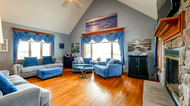 living room featuring high vaulted ceiling, a stone fireplace, and hardwood / wood-style flooring