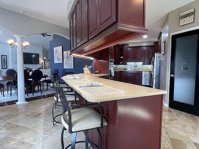 kitchen featuring stone tile floors, decorative columns, ceiling fan, a peninsula, and light countertops