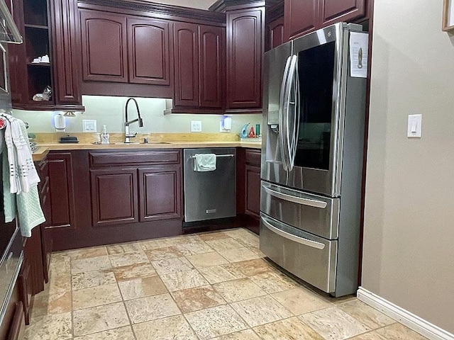 kitchen featuring stainless steel appliances, a sink, baseboards, light countertops, and stone finish floor