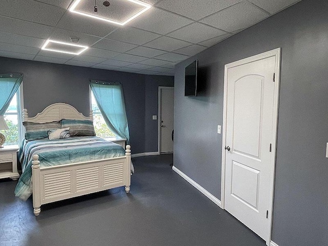 bedroom with concrete flooring, a drop ceiling, baseboards, and multiple windows